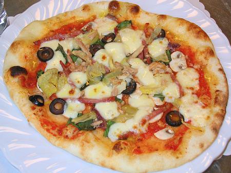выпек пиццу, увенчанную помидорами, сыром Моцарелла и свежим базиликом